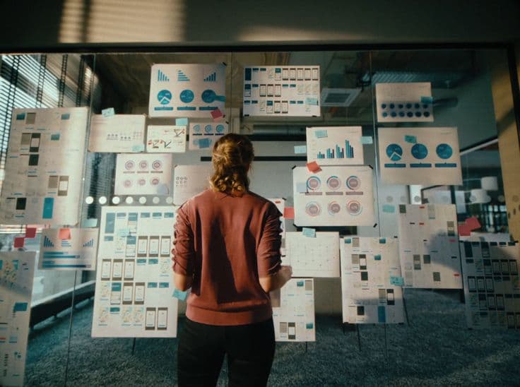 A person reviewing printed charts and wireframes on a glass wall