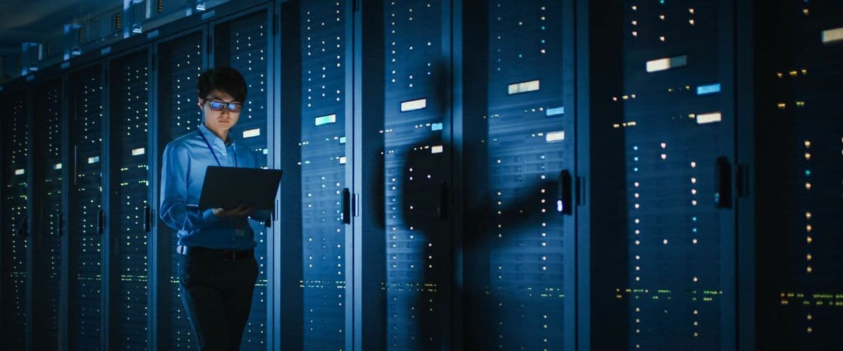 A person reviewing a laptop in a server room lined with data racks